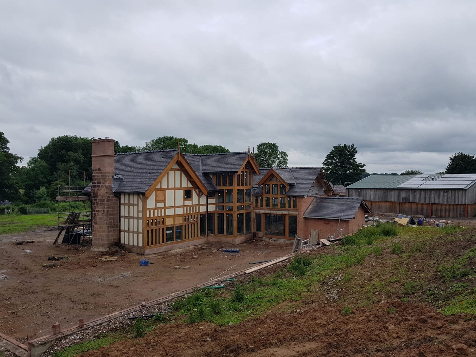 Oak-framed extension nearing completion with sandstone chimney and slate roof