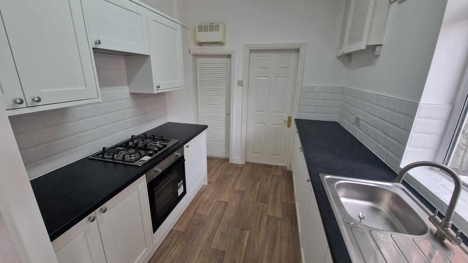 Finished galley kitchen with white shaker units and black worktops